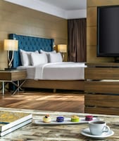 Una camera d'albergo con un letto, comodini, una TV e un tavolo con pasticcini e una tazza.