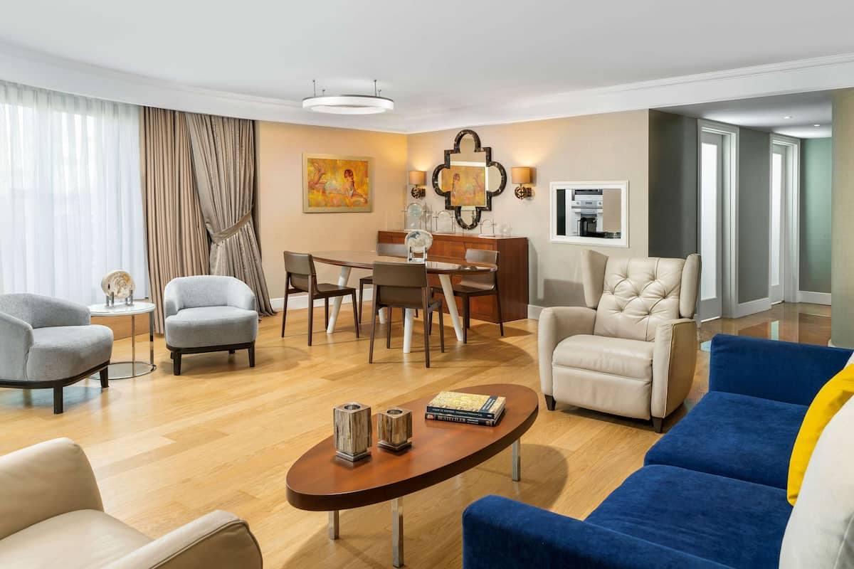A modern living room with a dining area, featuring a round table, two armchairs, a sofa, and a coffee table.