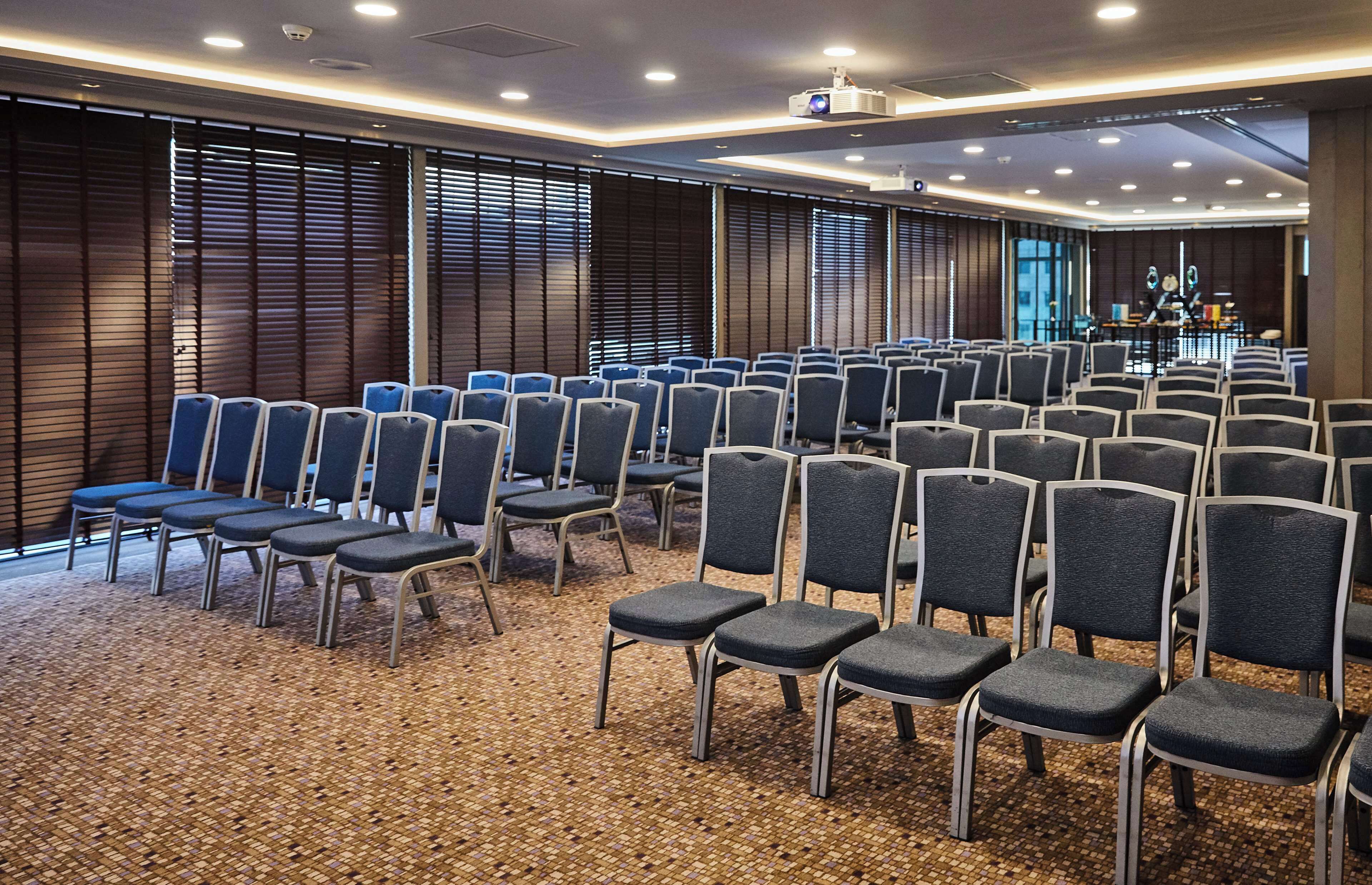 A conference room with rows of chairs, a projector, and a stage.
