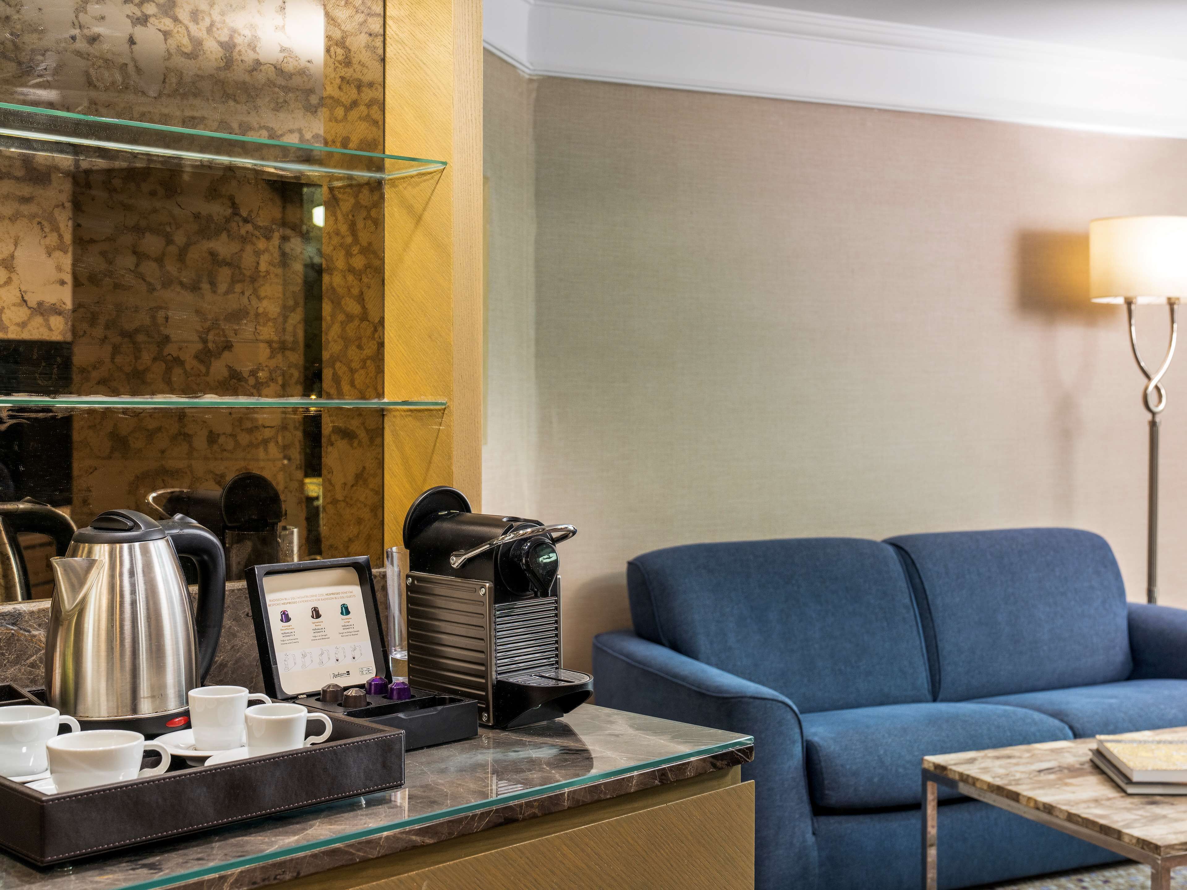 A hotel room with a marble countertop, a coffee station, a sofa, and a lamp.