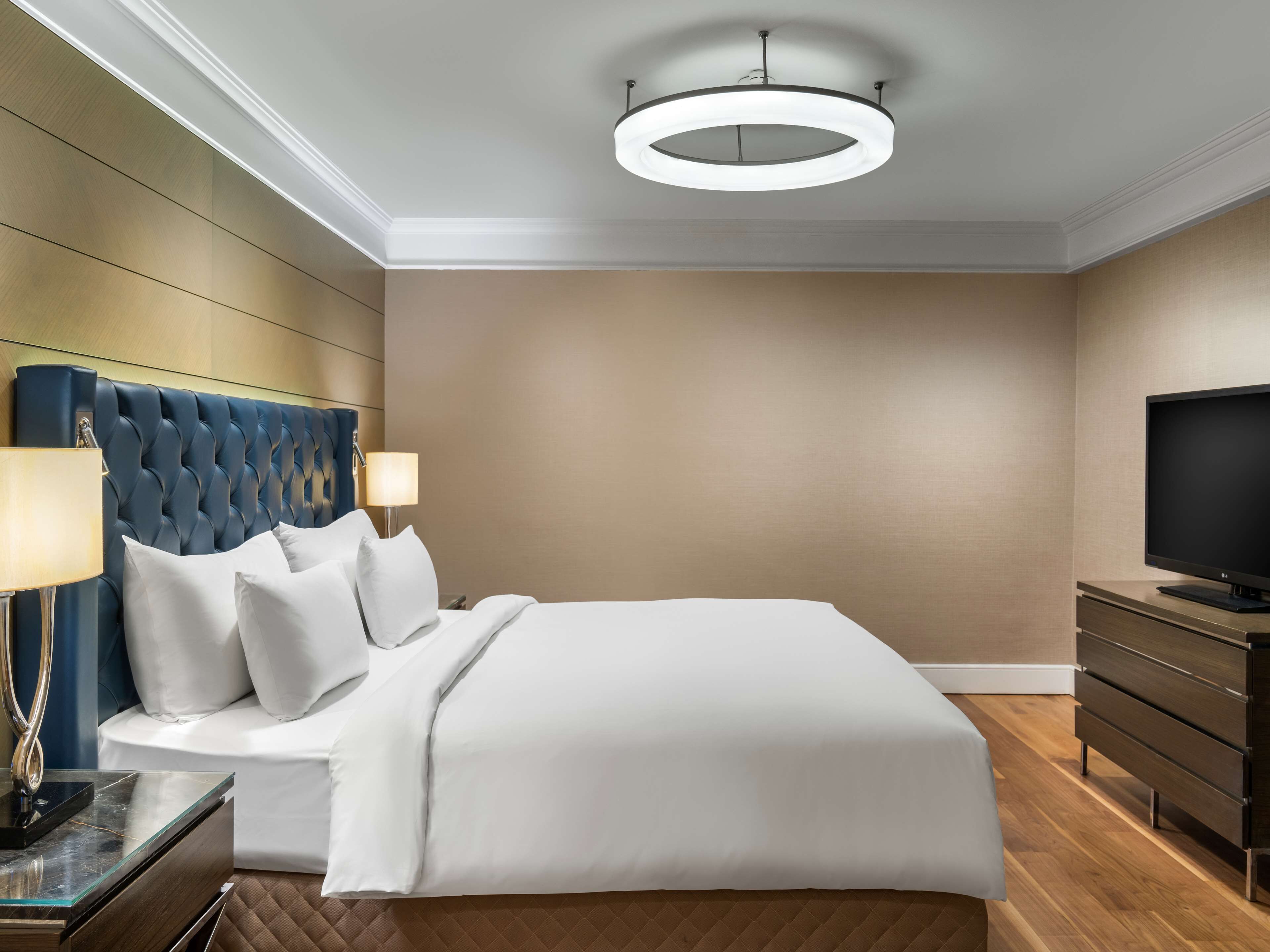 Una habitación de hotel con una cama grande, televisión, cómoda y una lámpara de techo moderna.