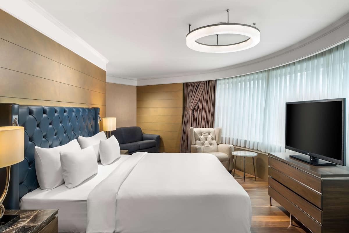A hotel room with a large bed, a TV, a desk, and a chair.