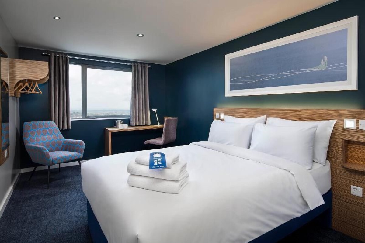 Une chambre d’hôtel avec un grand lit, deux fauteuils, un bureau et une fenêtre donnant sur un beau paysage.