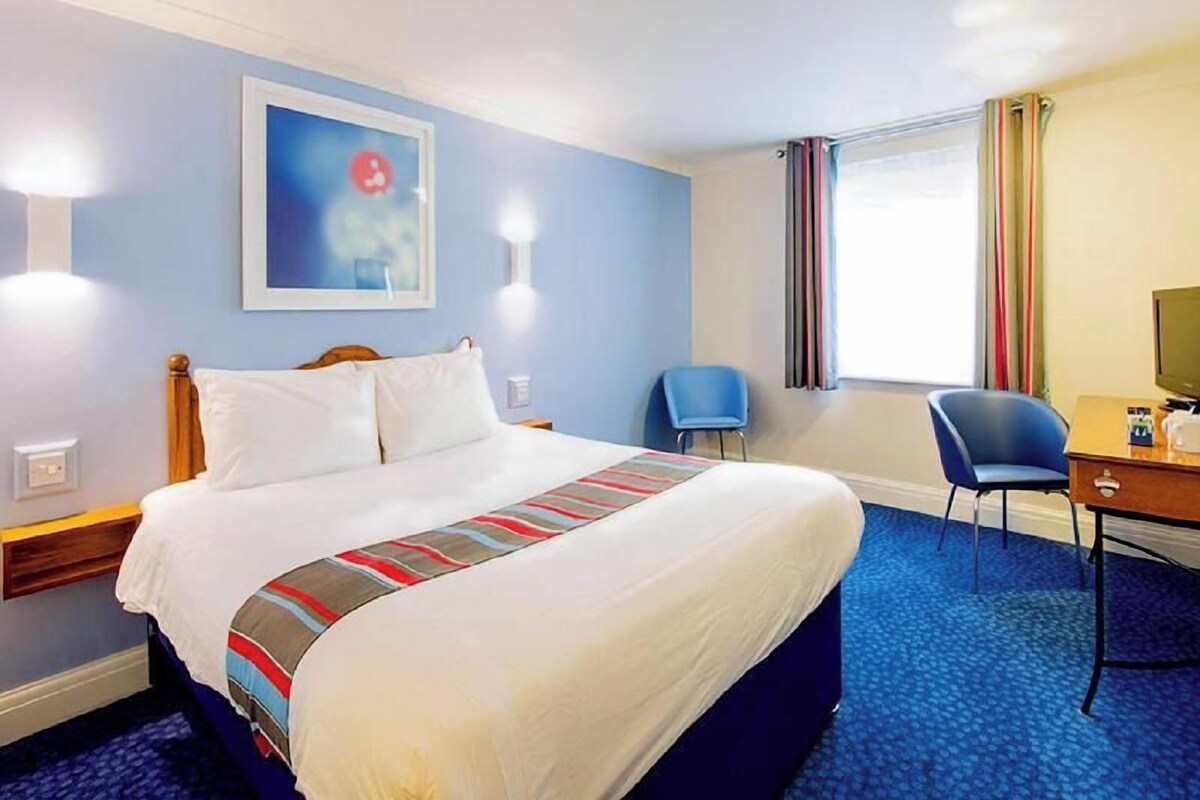 A hotel room with a bed, a desk, a chair, a television, and a window with curtains.