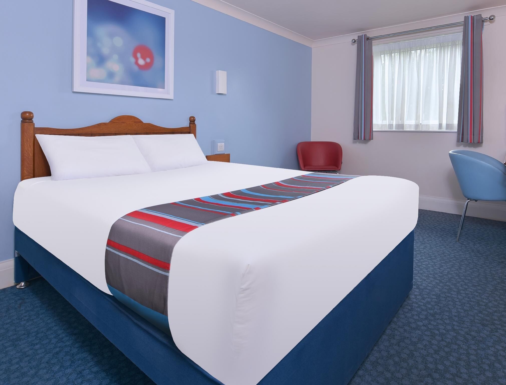 A hotel room with a large bed, a desk, a chair, a window with curtains, and a wall-mounted picture.
