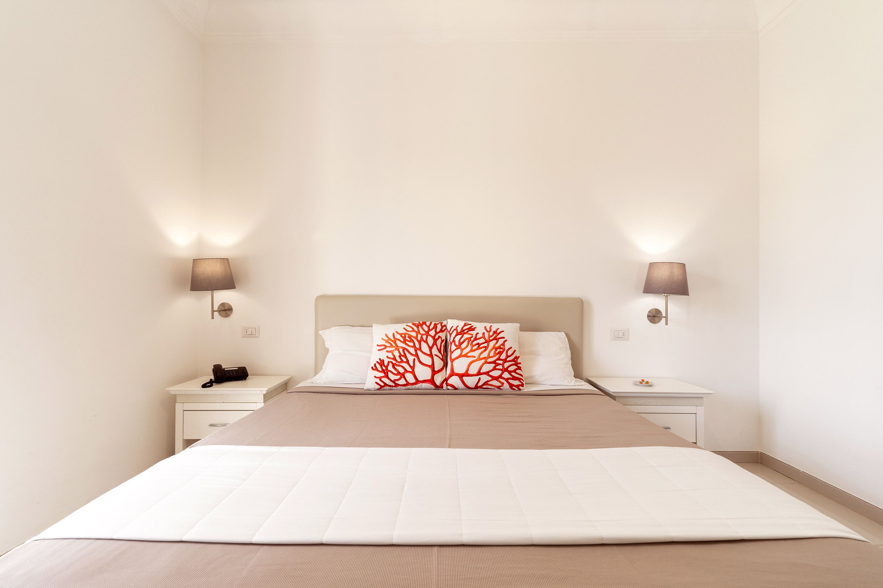 A neatly arranged bedroom with a large bed, two bedside tables, and a nightstand with a lamp.