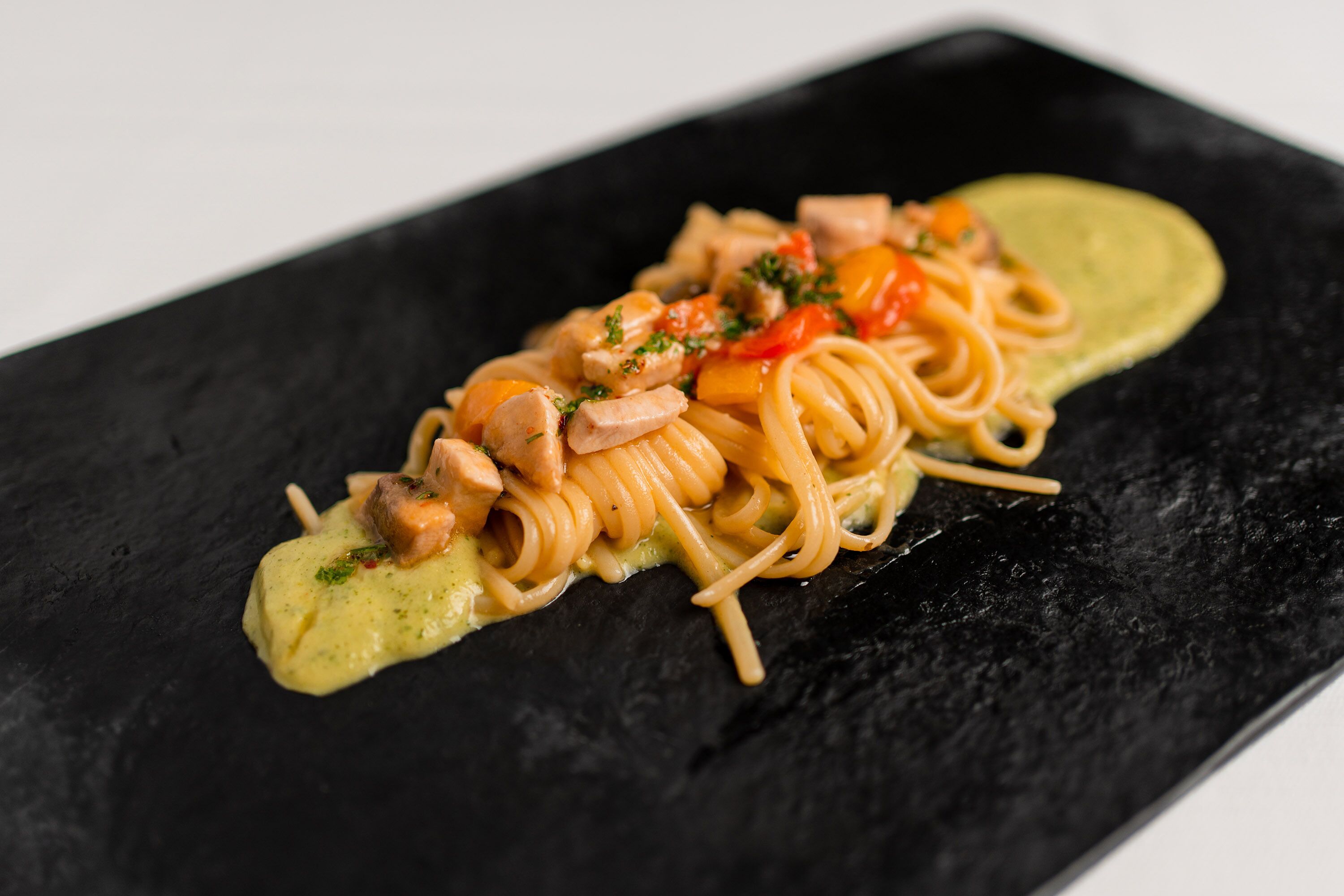 Spagettia, kanaa ja kasviksia sisältävä annos tarjoiltuna mustalla lautasella.