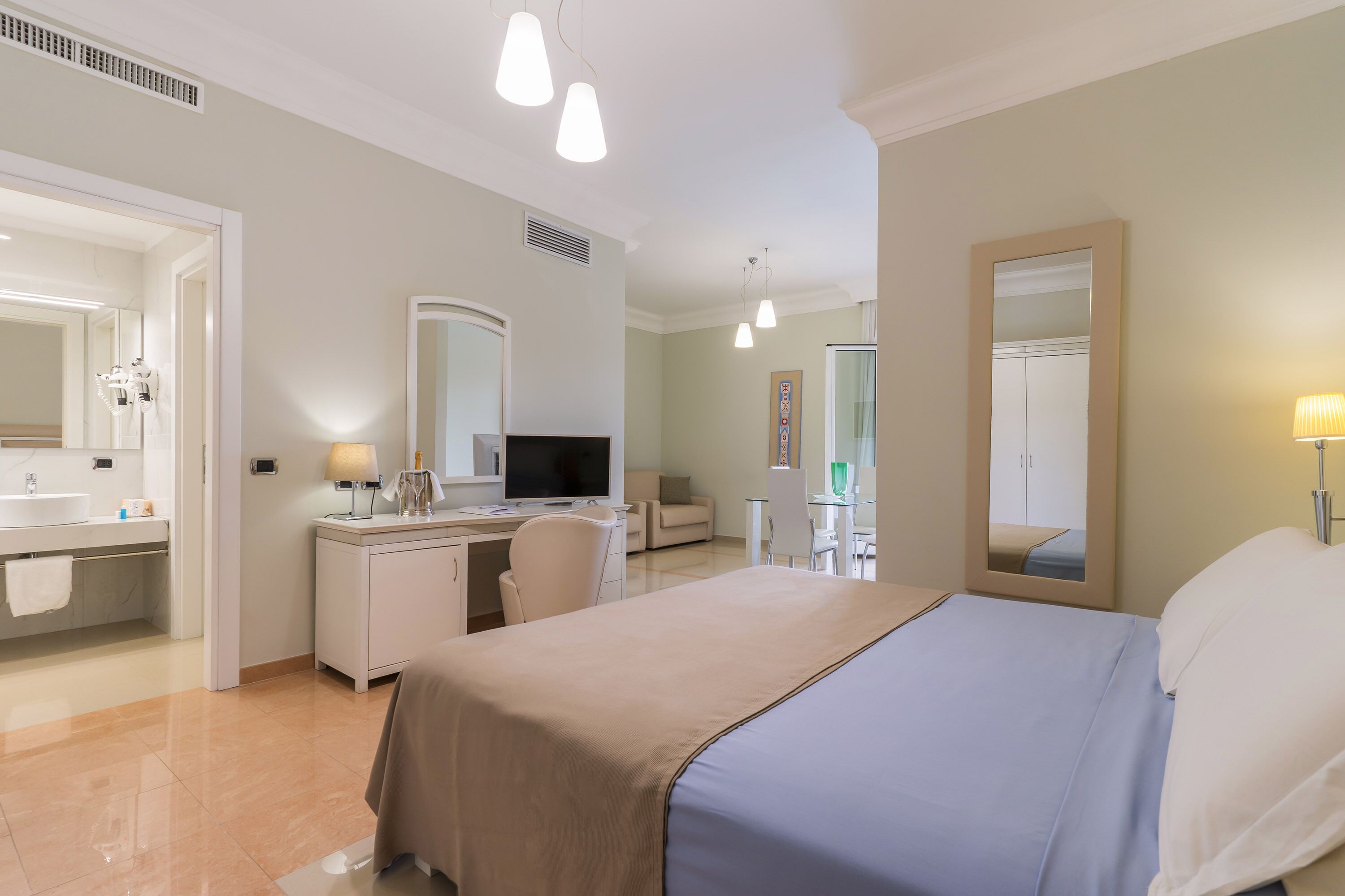 A hotel room with a bed, a desk, a chair, a television, a mirror, and a bathroom with a sink and toilet.