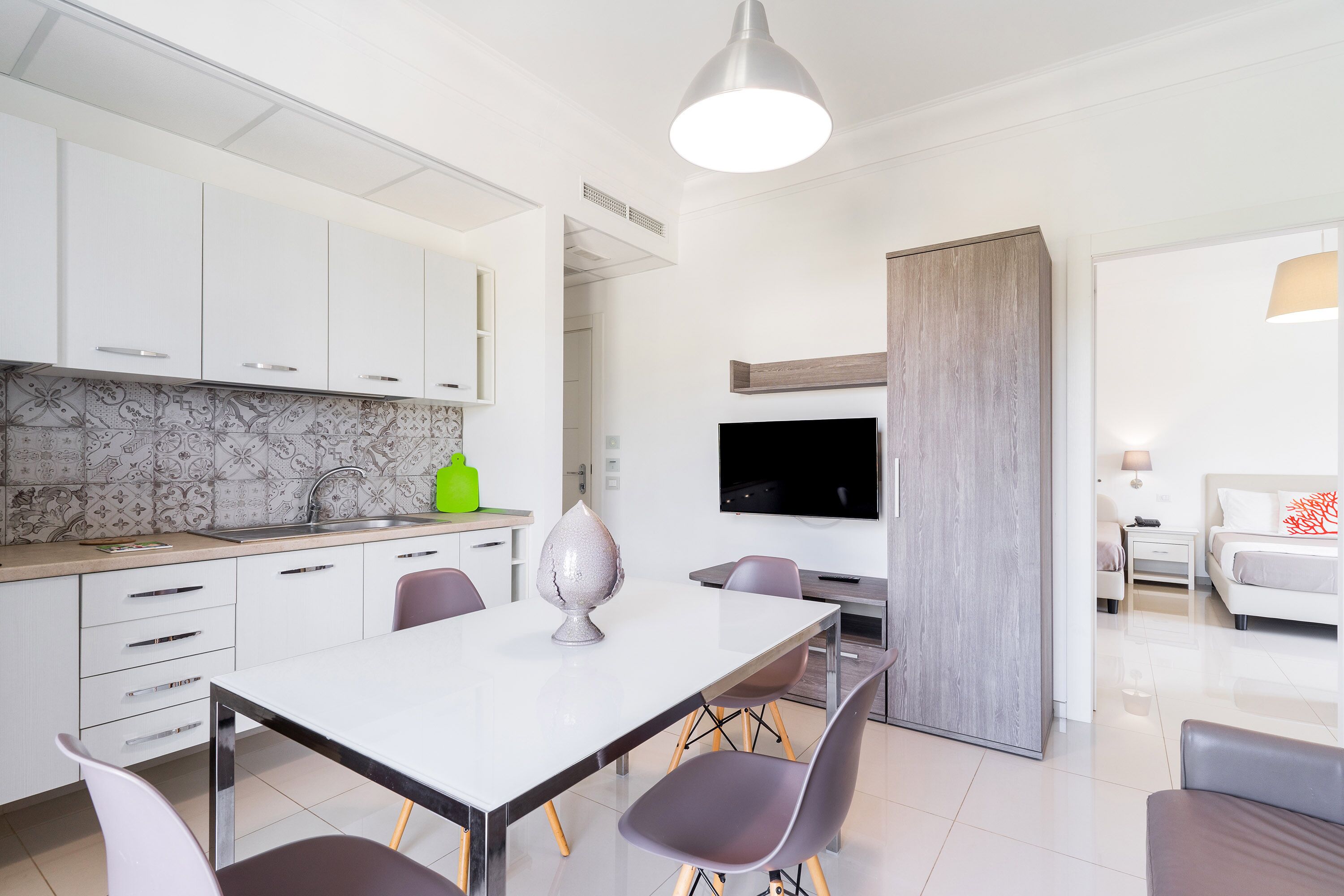 Une cuisine moderne avec des meubles blancs, un pare-feu en marbre et un coin repas comprenant une table et des chaises blanches.