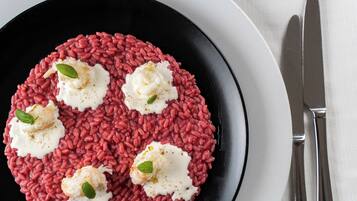 Un plato negro con risotto rojo y cucharadas de crema, adornado con hojas de albahaca.