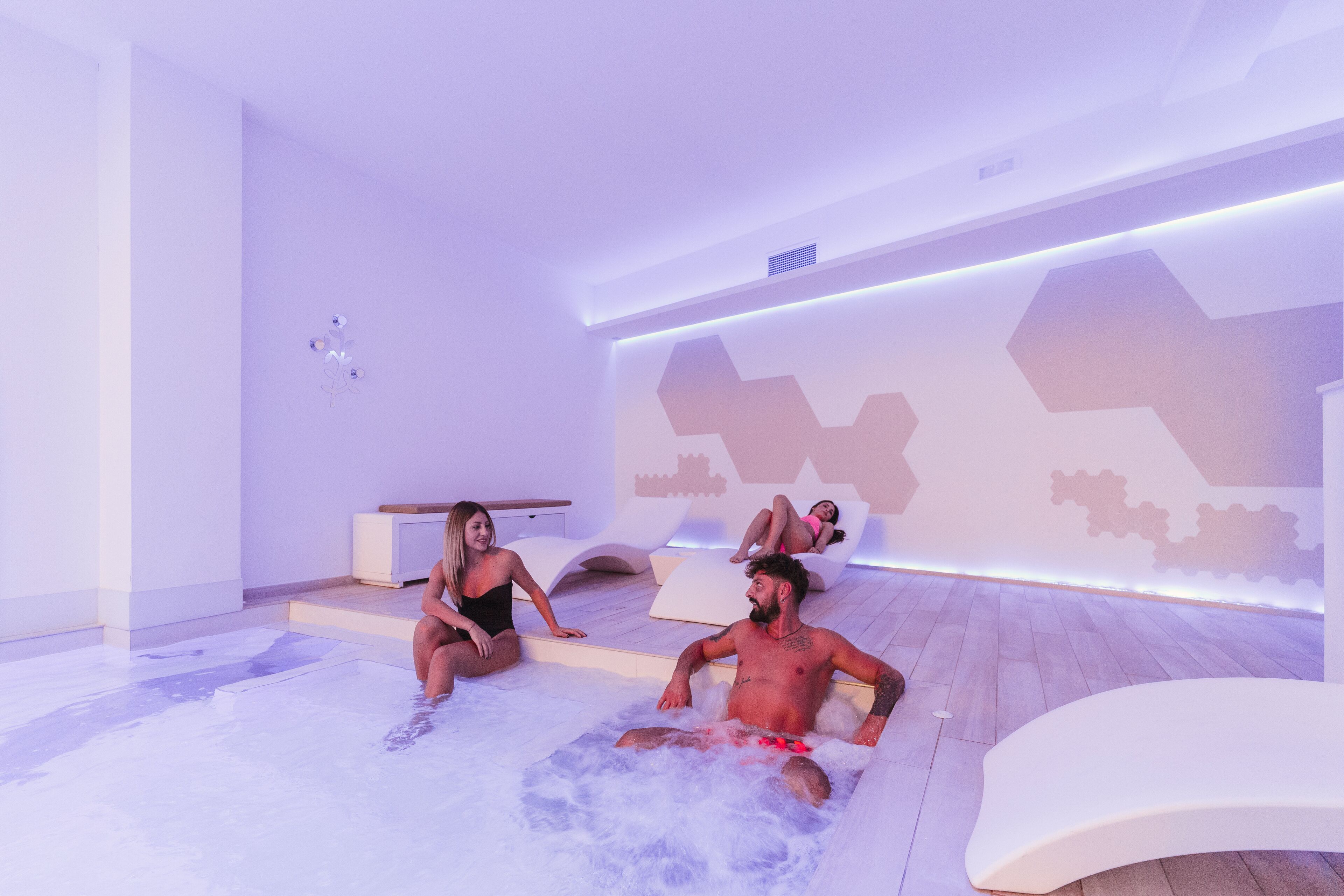 A modern spa room with a heated floor, a seating area, and a wall with geometric patterns.