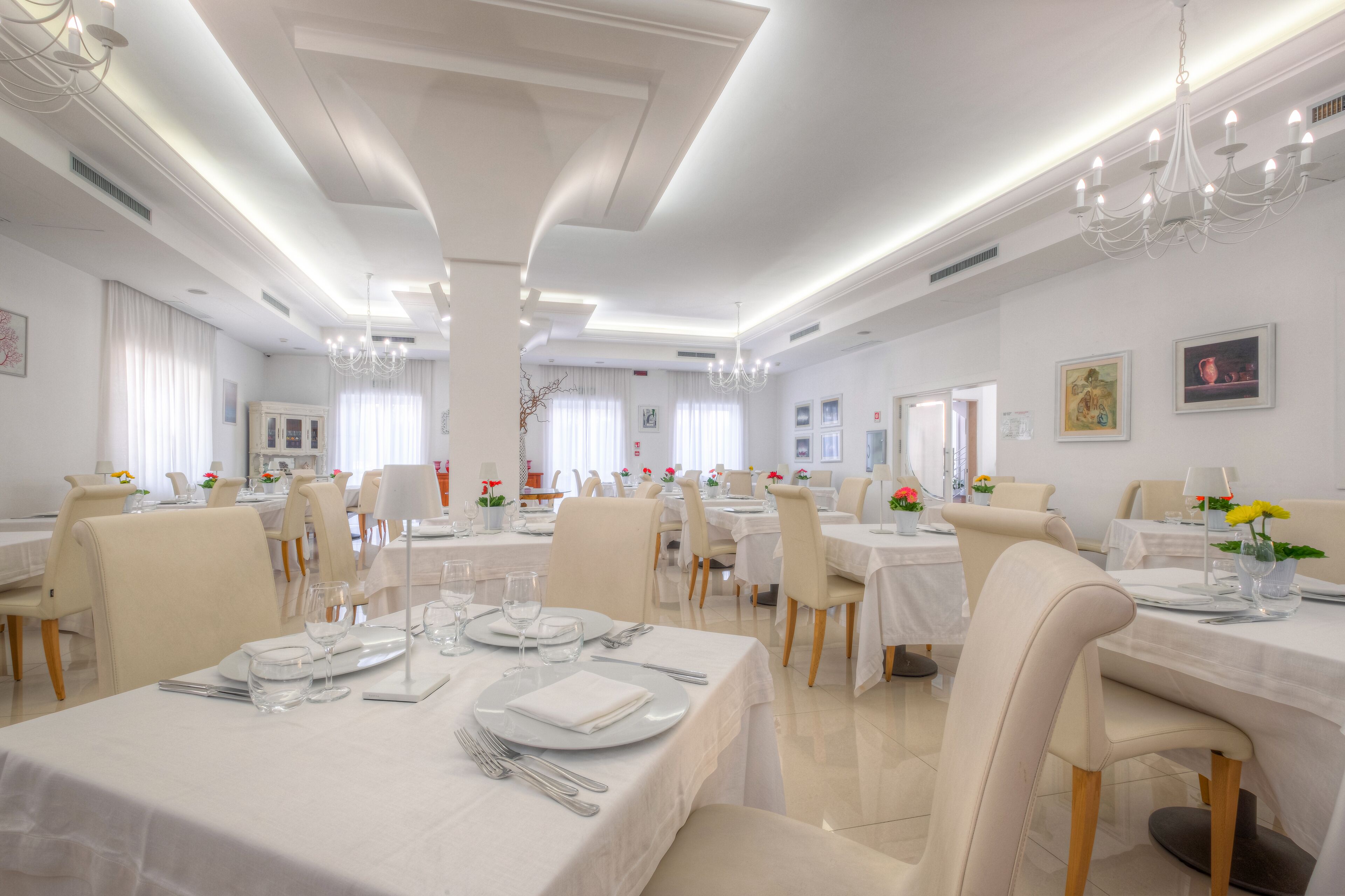 A spacious dining area with multiple tables set for dining, featuring white tablecloths and chairs.