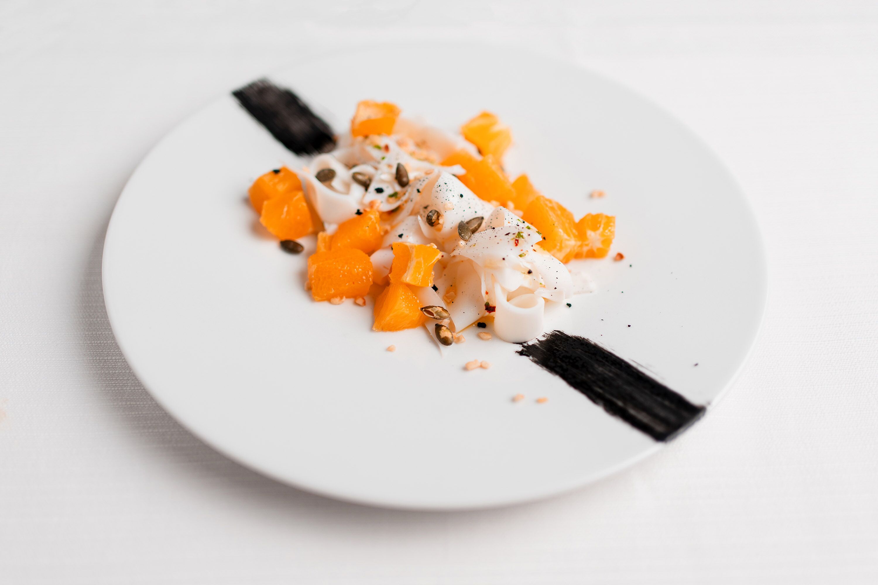 A white plate with a dessert consisting of orange segments and white cream, garnished with seeds.