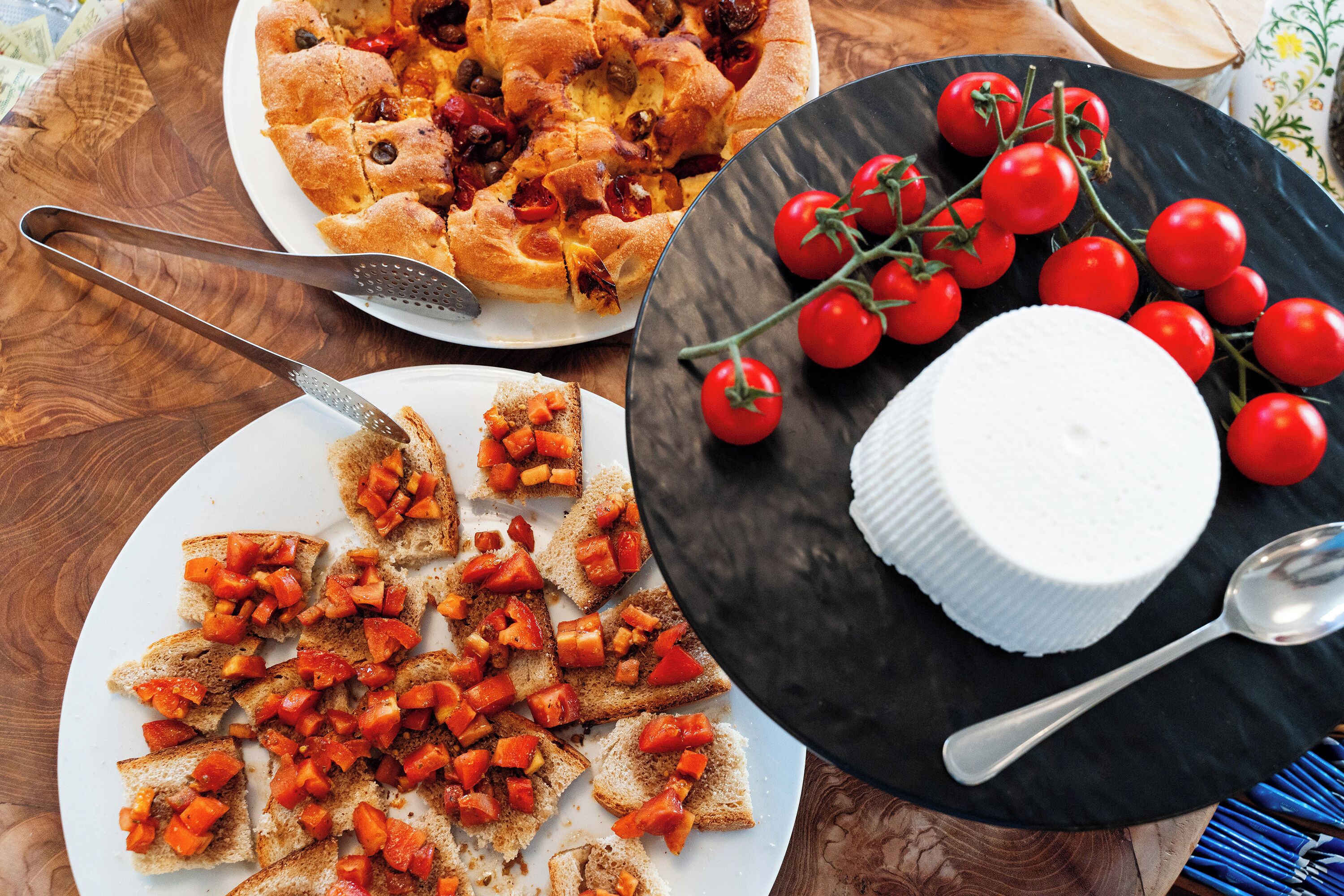 Una mesa con una pizza, una fuente de bruschetta y un queso entero.