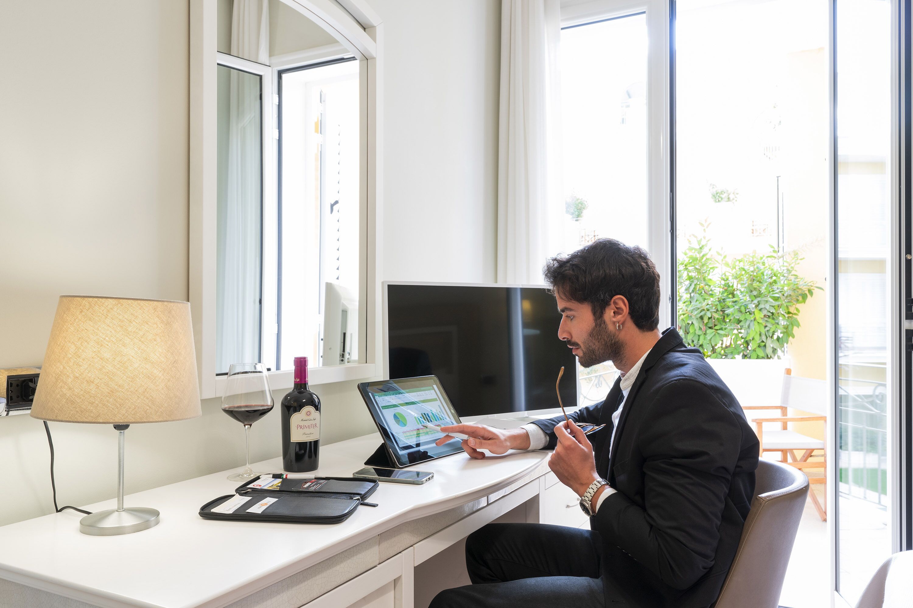 A man sitting at a desk with a laptop, a wine bottle, and a glass of wine.