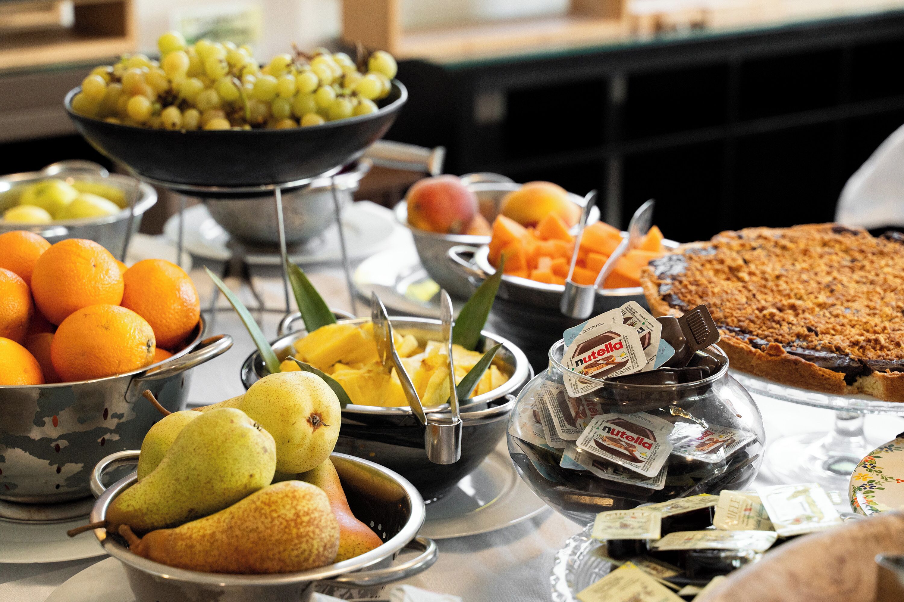 A buffet with various fruits, including oranges, pears, and mangoes, and a chocolate dessert.