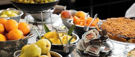 A buffet with various fruits, including oranges, pears, and mangoes, and a chocolate dessert.