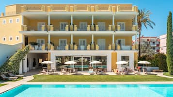 A multi-story hotel with a swimming pool, outdoor seating, and a well-maintained lawn.