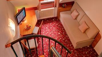 A cozy room with a sofa, a small table with a bowl of fruit, a TV, and a staircase.