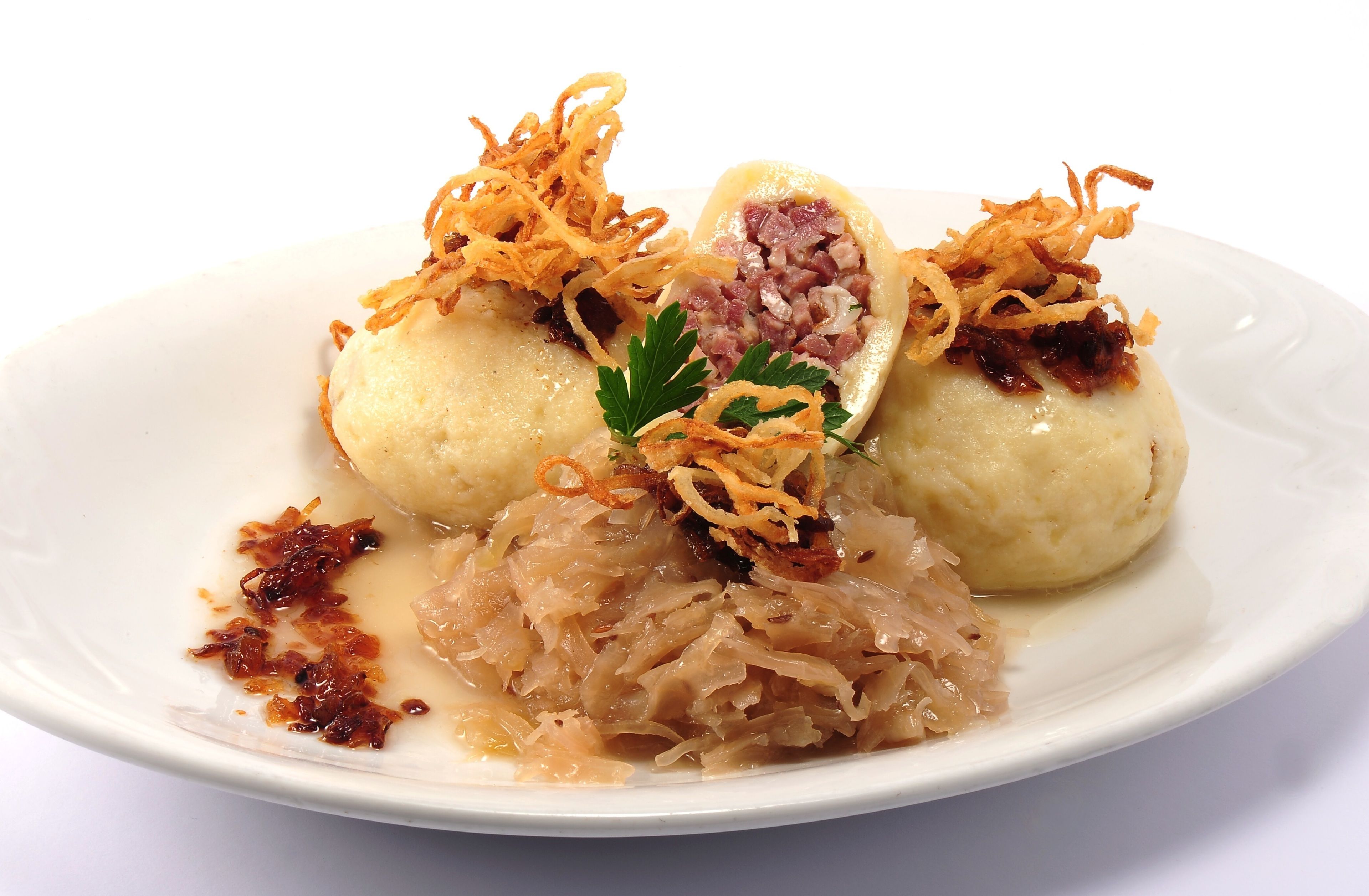 A plate of dumplings with a garnish of fried onions and a side of sauerkraut.