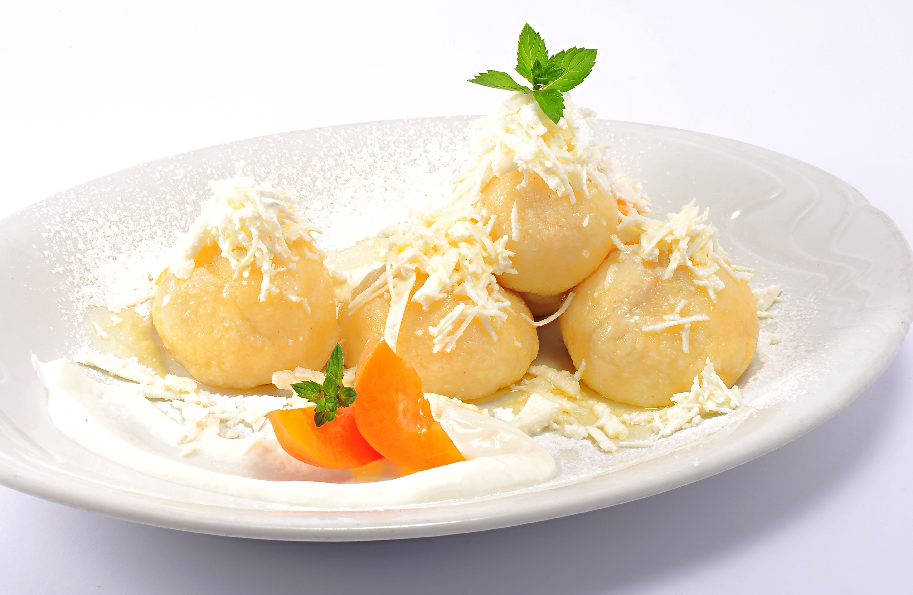 Une assiette de boulettes rondes, de couleur pâle, garnies de fromage râpé et d’une feuille de menthe, accompagnée d’une cuillerée de crème et d’une tranche d’orange.