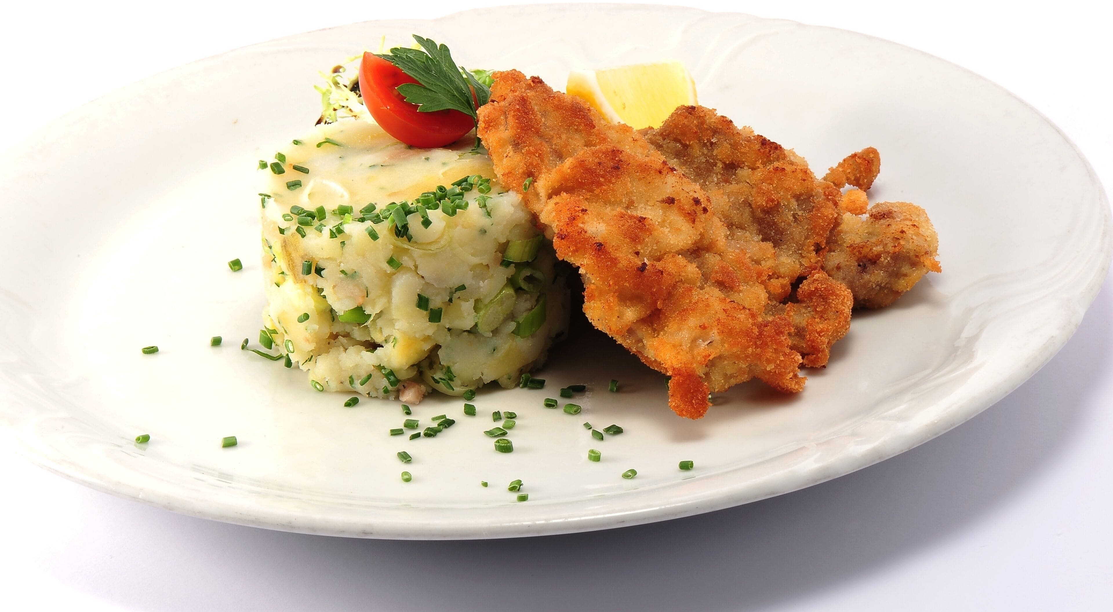 Une assiette comprenant une escalope panée, de la purée de pommes de terre et une garniture de ciboulette.