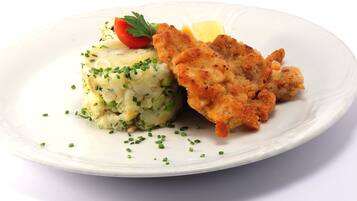 Une assiette comprenant une escalope panée, de la purée de pommes de terre et une garniture de ciboulette.