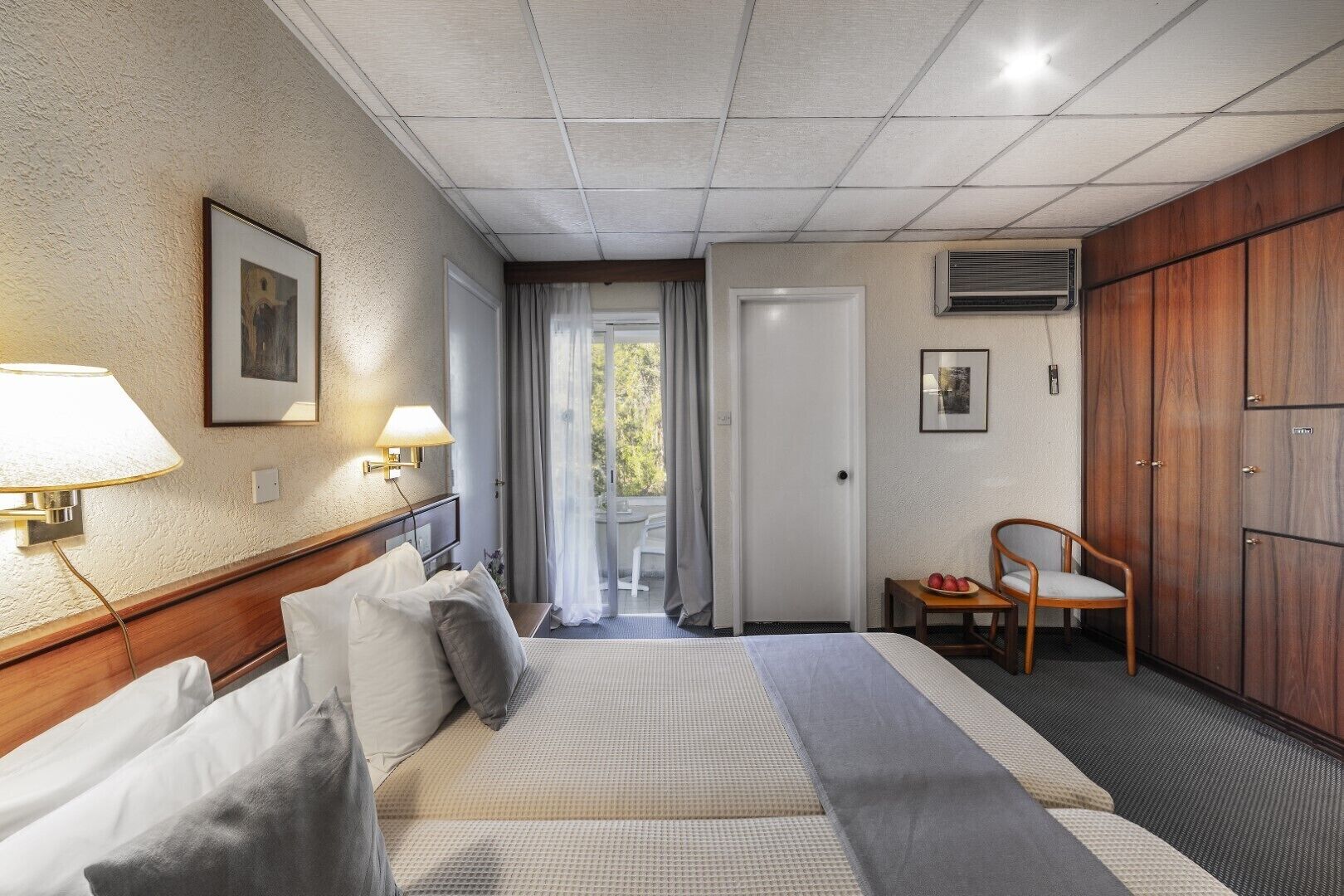 Habitación de hotel con cama, una silla, armario y puerta que da a un balcón.