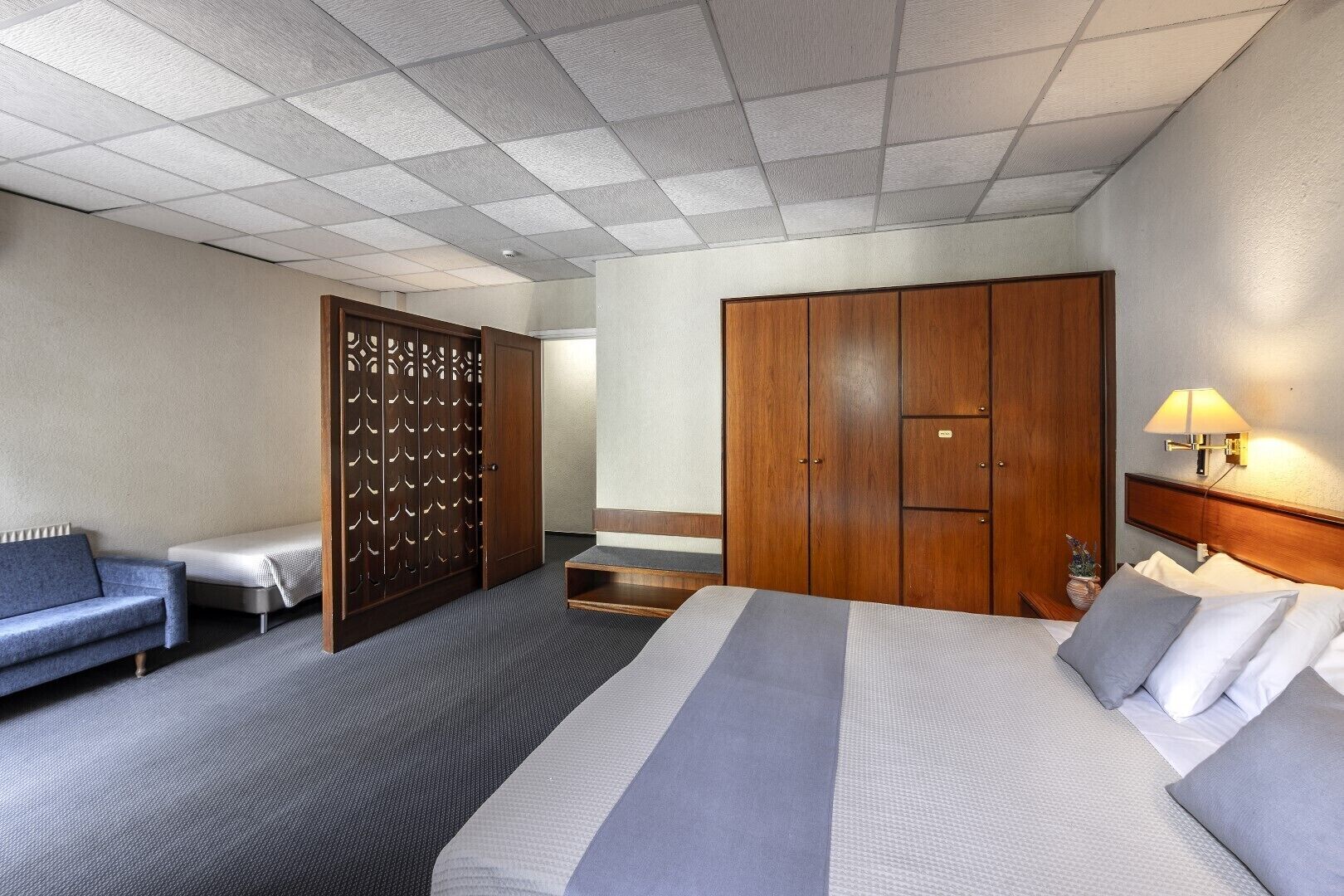A hotel room with a bed, a sofa, a wardrobe, and a desk.