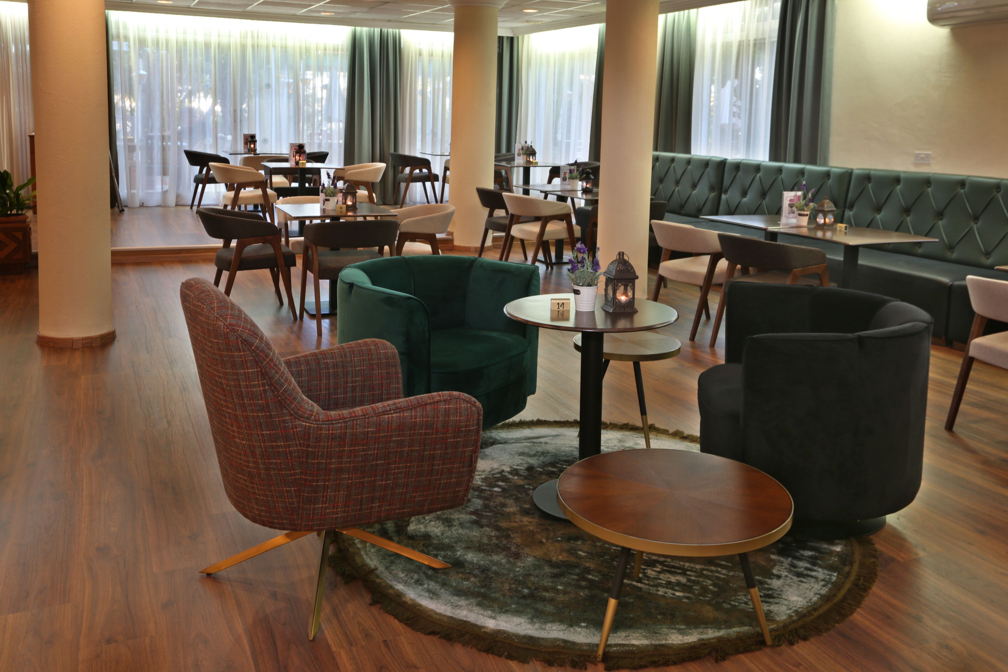 A modern hotel lobby with wooden flooring, green upholstered seating, and a variety of tables and chairs.