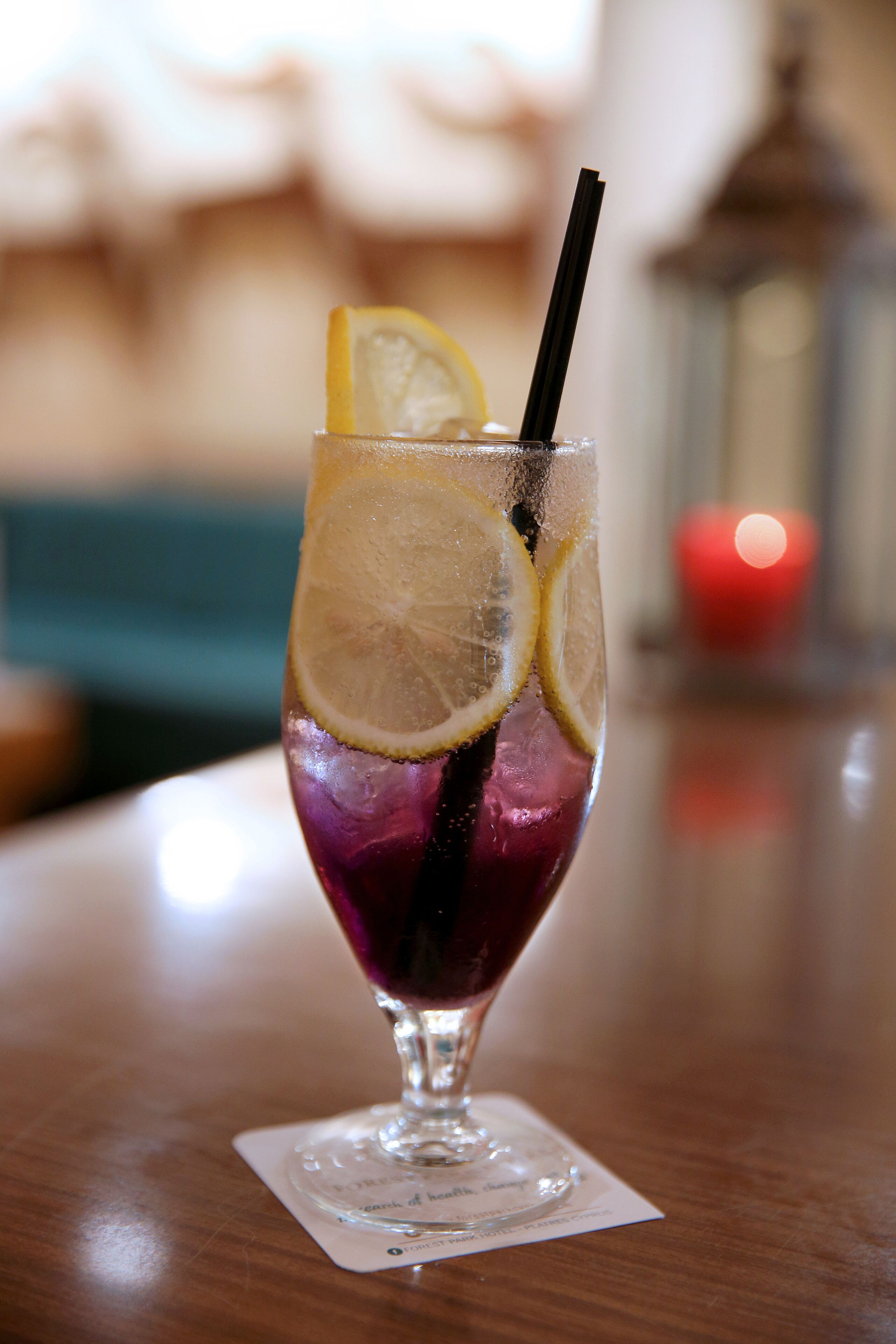 A glass with a dark-colored beverage, lemon slices, and a straw on a wooden table.