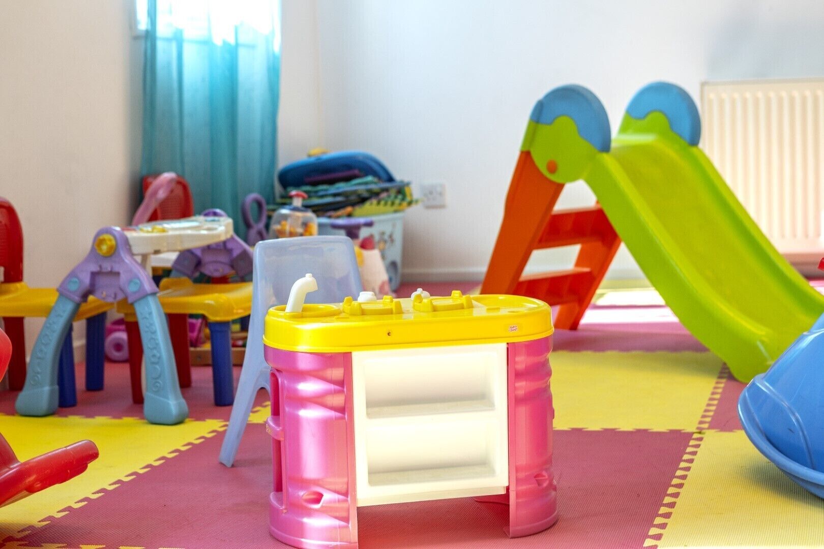 Een speelruimte voor kinderen met diverse speelgoed en een klein tafeltje met een gele deksel.