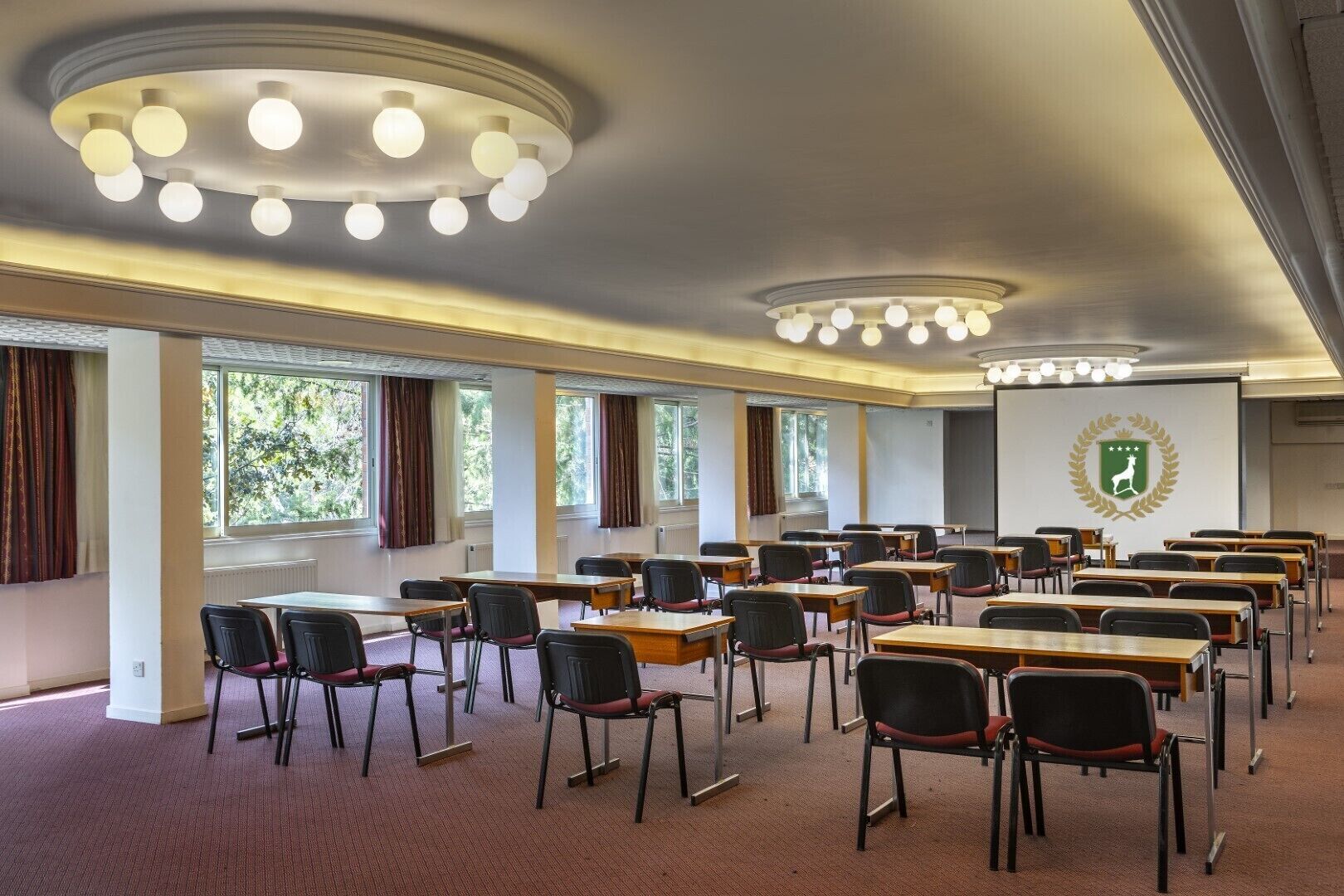 A conference room with multiple tables and chairs, large windows, and a ceiling light fixture.