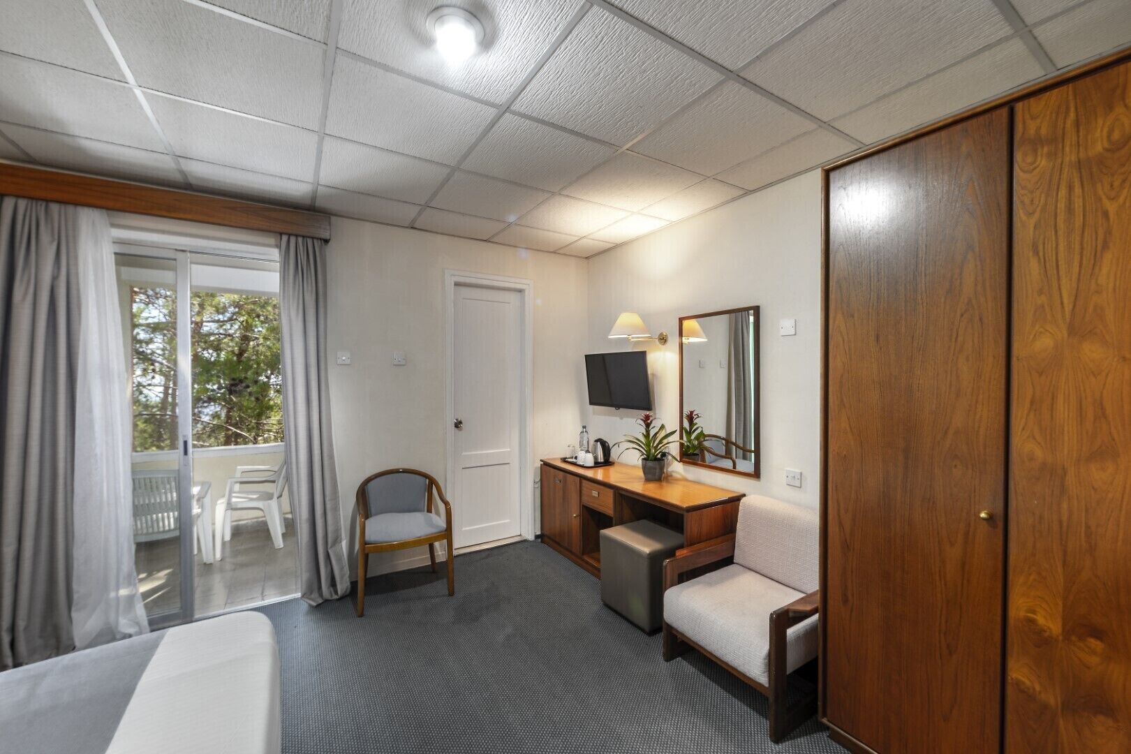 Una habitación de hotel con cama, escritorio con silla, televisor, espejo y armario.