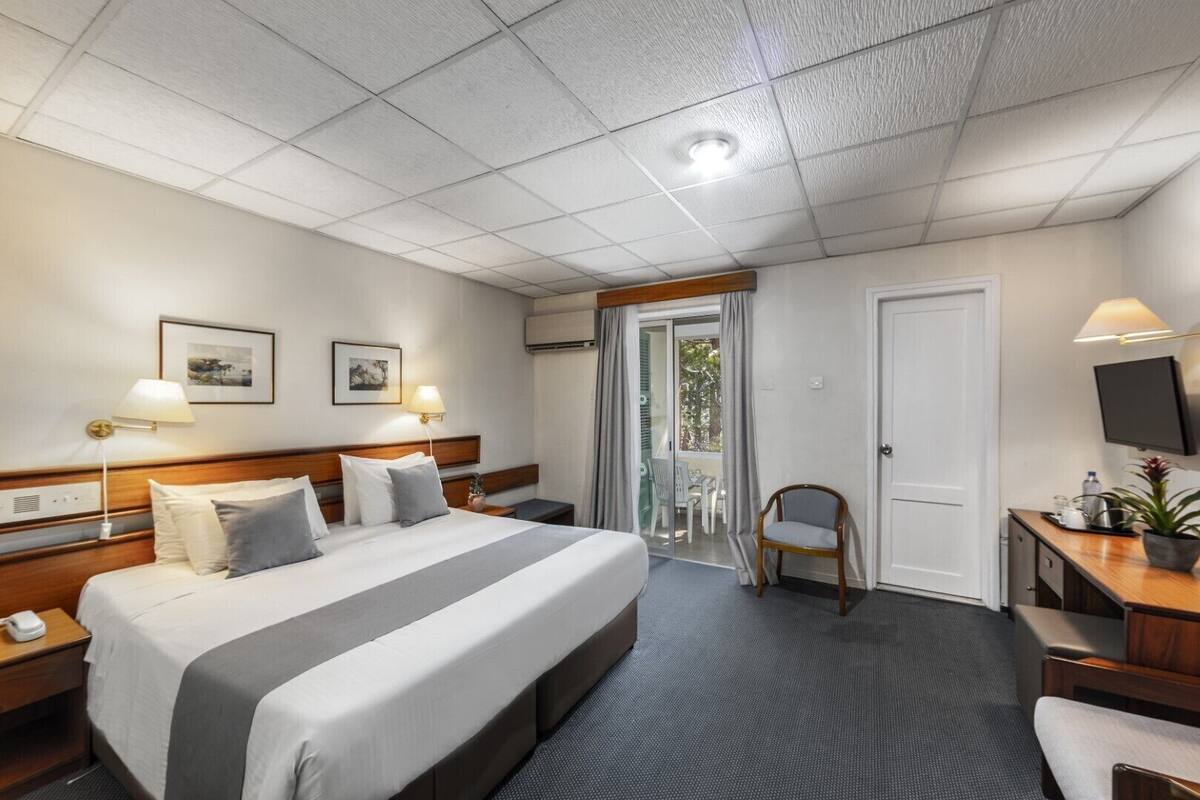 A hotel room with a large bed, bedside tables, a desk with a chair, a TV, and a balcony with chairs.