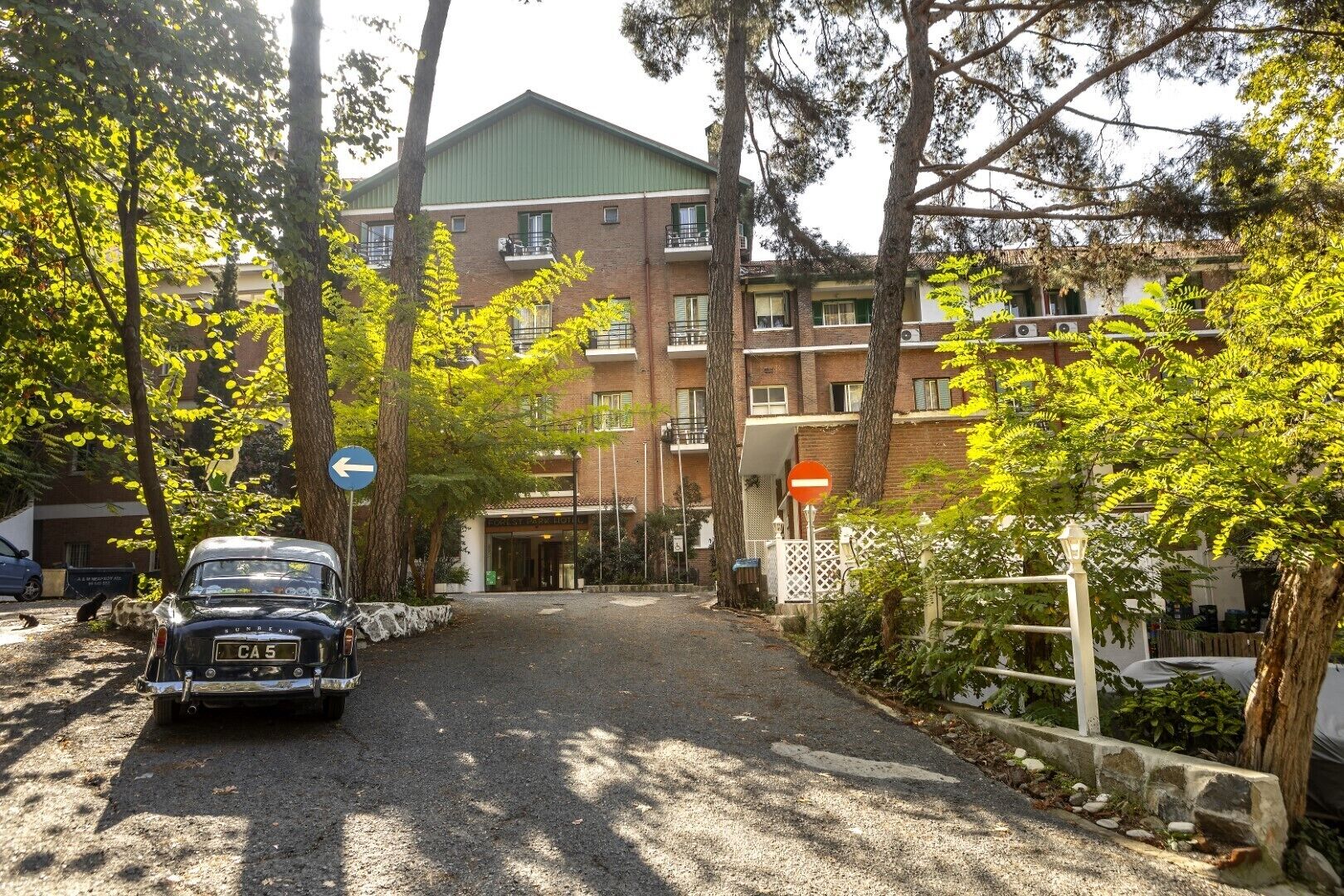 A building with a green roof, a gravel driveway, and a car parked on the side.