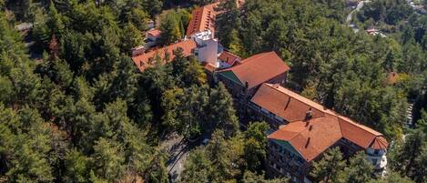 Vista aérea de un hotel rodeado de un bosque denso, con un edificio alargado de tejado rojo y varios balcones.