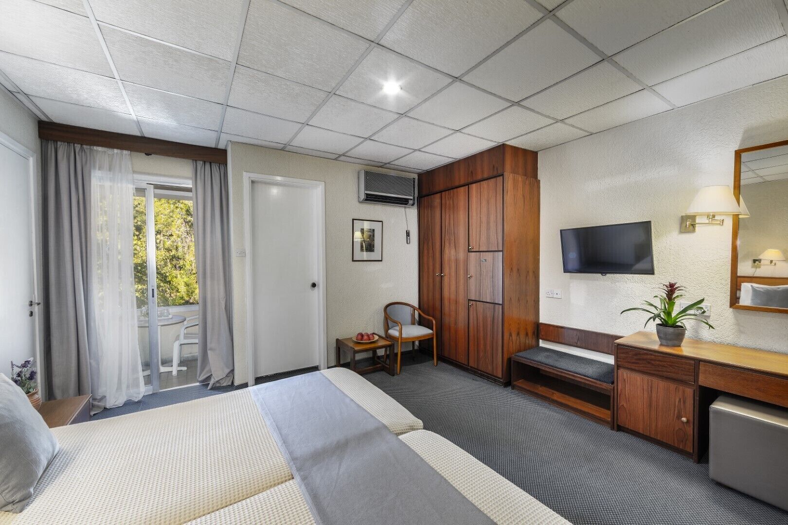 A hotel room with a bed, a desk, a chair, a TV, and a window with curtains.