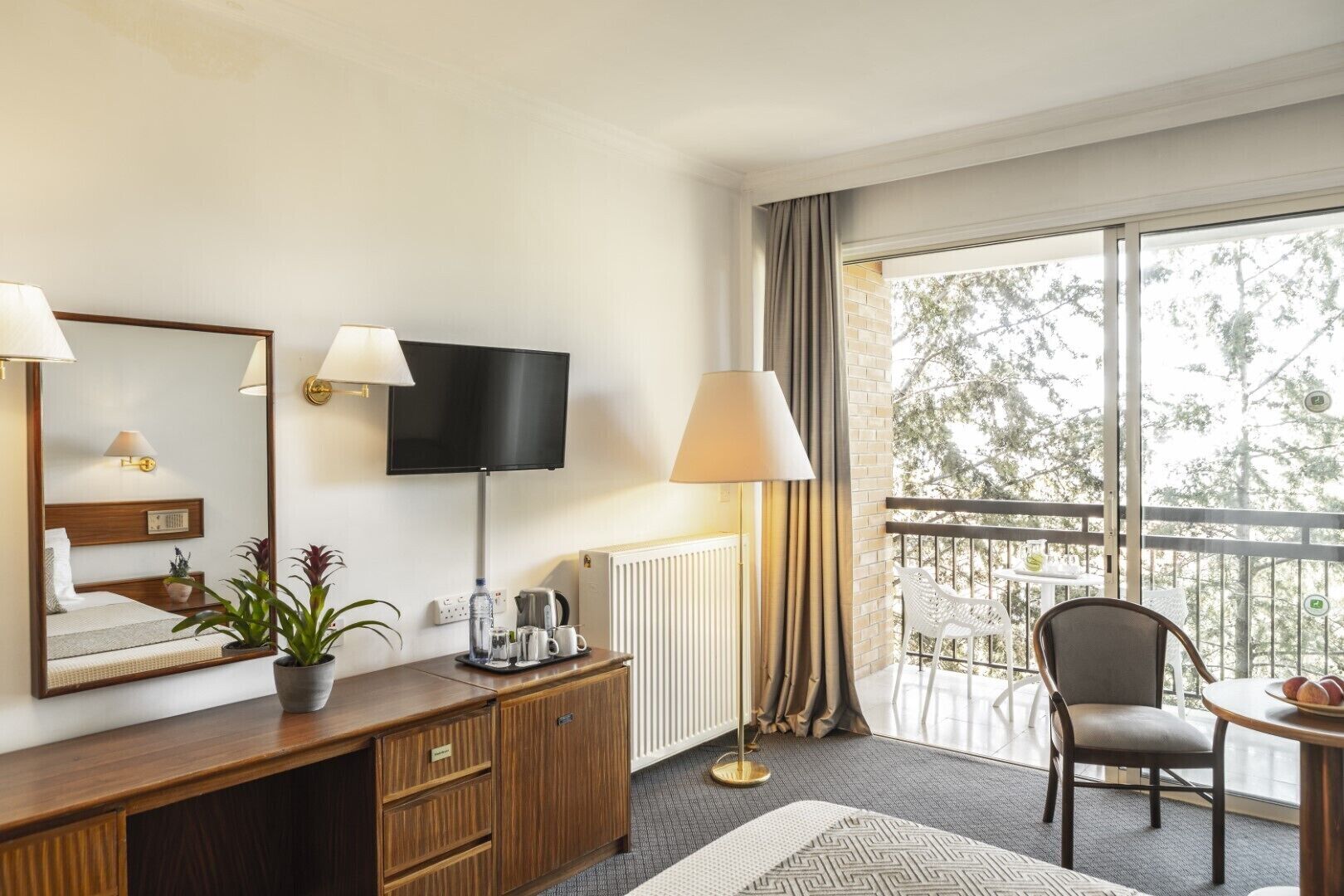 A hotel room with a bed, bedside table, TV, and a balcony with a chair and table.