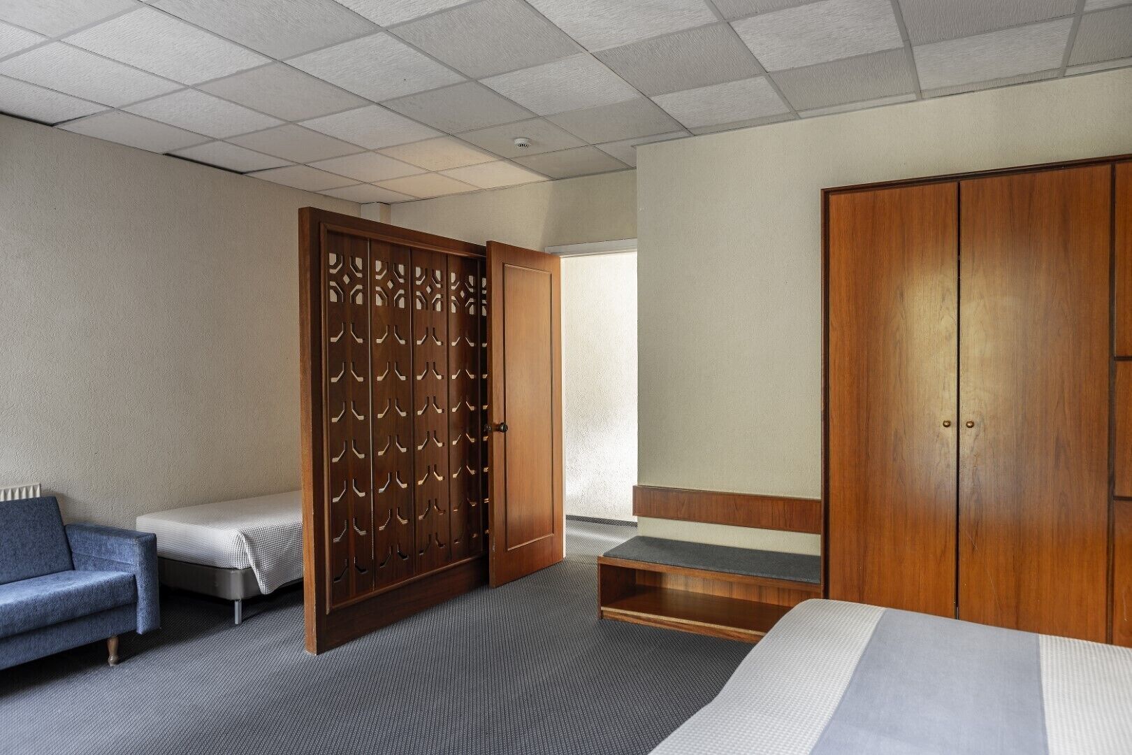 Habitación de hotel con cama, sofá, armario de madera y separador decorativo.