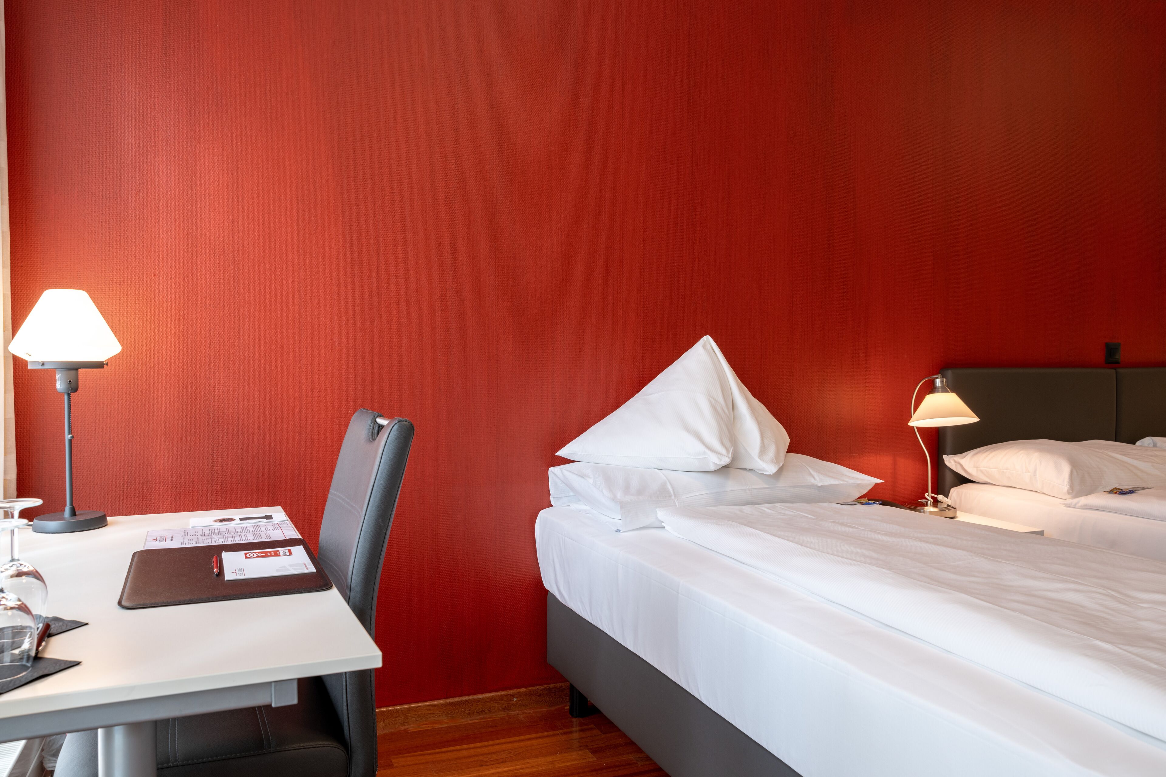 A hotel room with a bed, a desk with a lamp, and a chair.