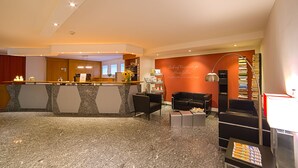 A hotel lobby with a reception desk, seating area, and a bookshelf.