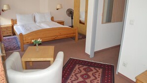 A bedroom with a wooden bed, bedside tables, a fan, a mirror, and a small table with a vase. - Hotel Pension Walzerstadt (Vienna)