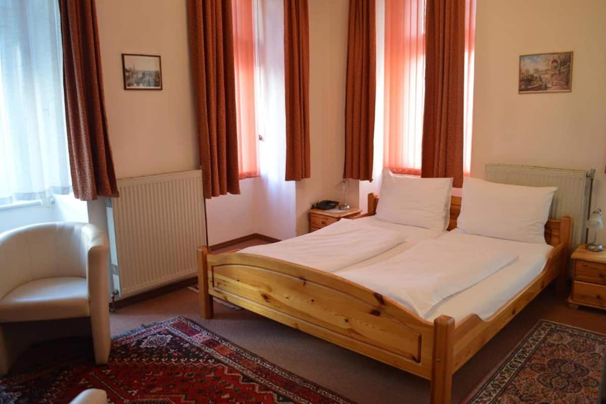 A bedroom with a wooden bed, a chair, a nightstand, and a radiator.