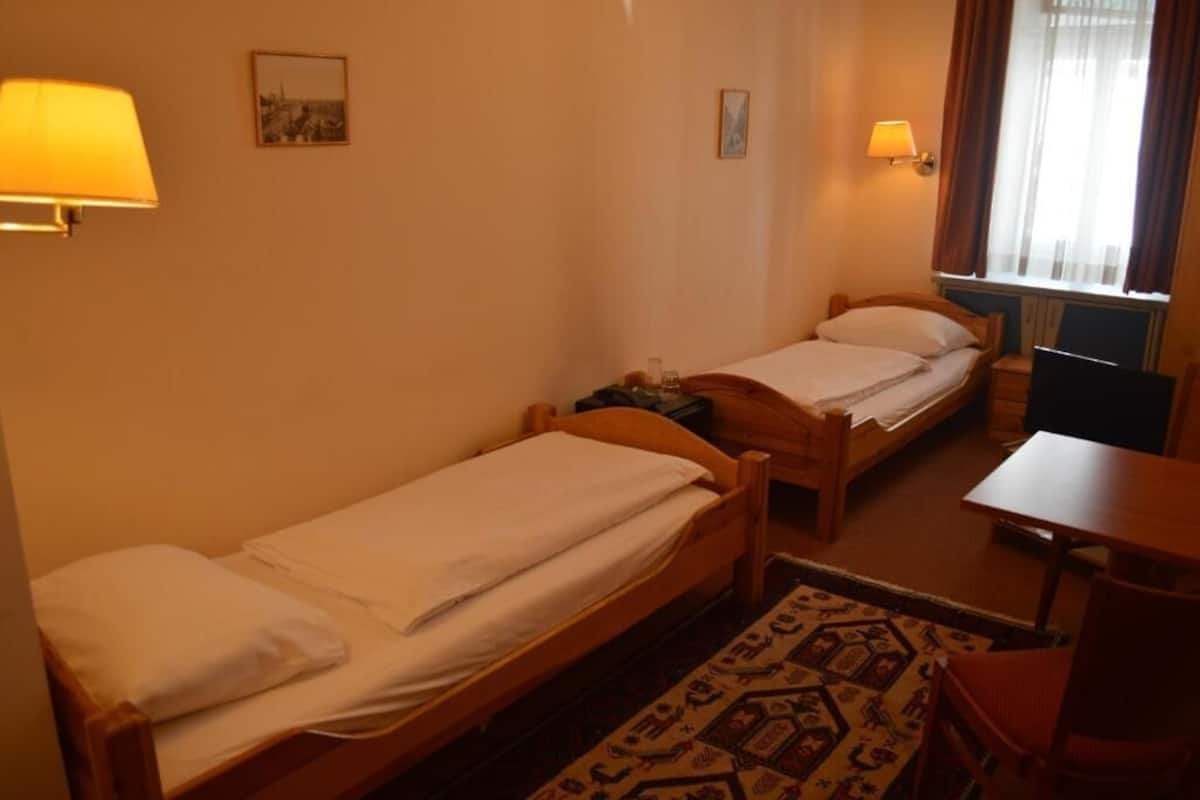 A small hotel room with two single beds, a desk, and a chair.
