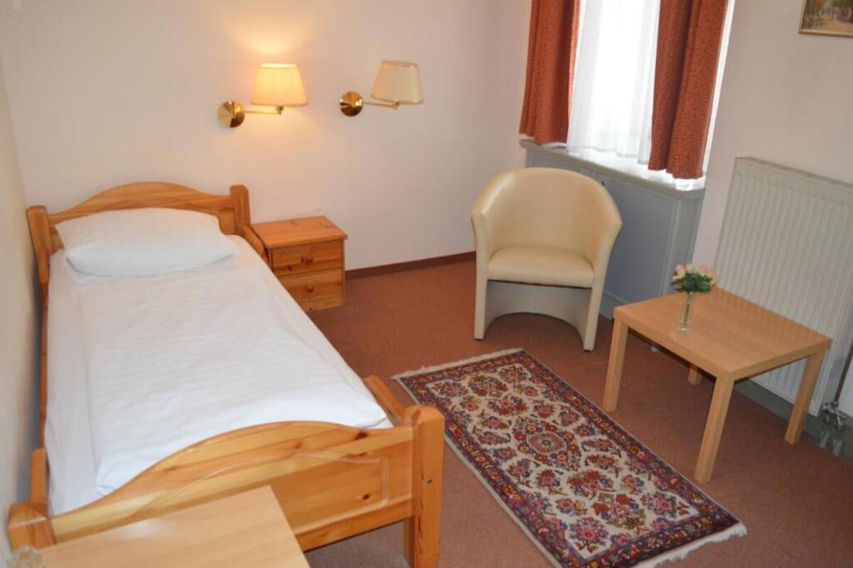 A bedroom with a wooden bed, bedside table, chair, and a small table with a vase.