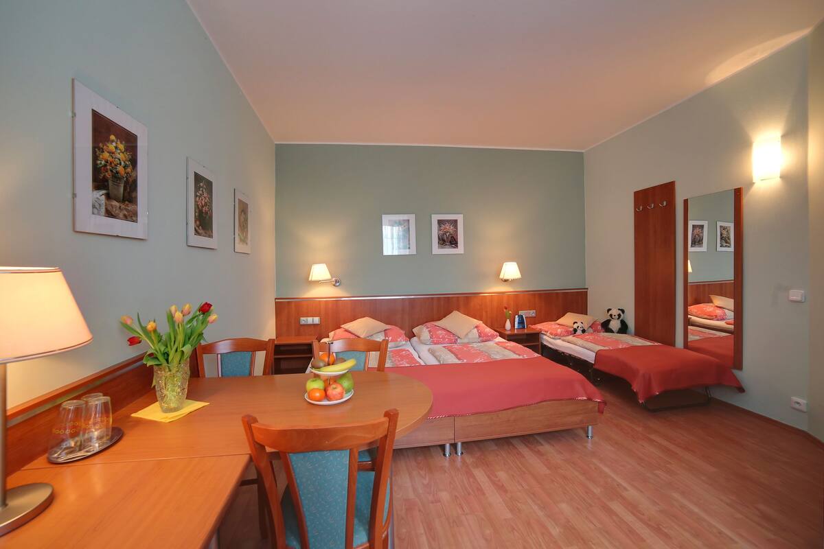 Quarto de hotel com cama de madeira, mesa de jantar com cadeiras, um vaso com flores e luminárias na parede.
