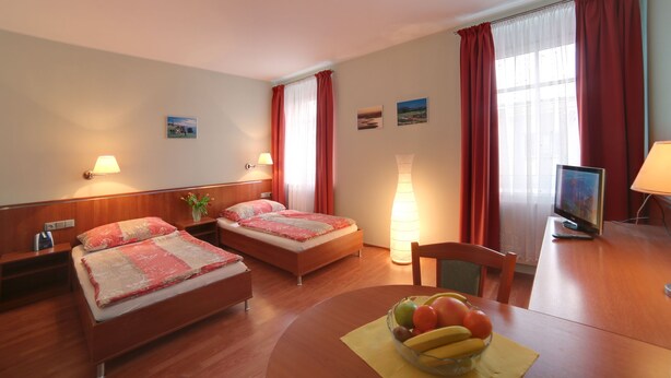 A hotel room with two beds, a dining table with fruit, a TV, and a lamp. - Penzion Fan (Karlovy Vary)