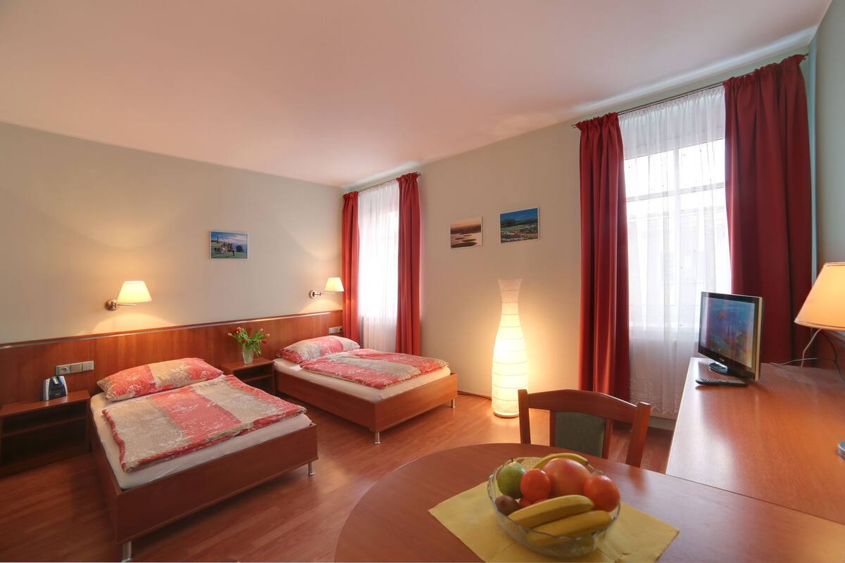 Quarto de hotel com duas camas, uma mesa de jantar com frutas, televisão e luminária.
