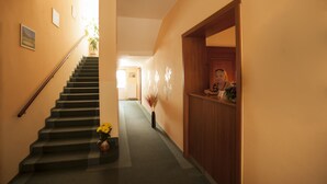 A hallway with a staircase, a wooden reception desk, and a vase with flowers. - Penzion Fan (Karlovy Vary)
